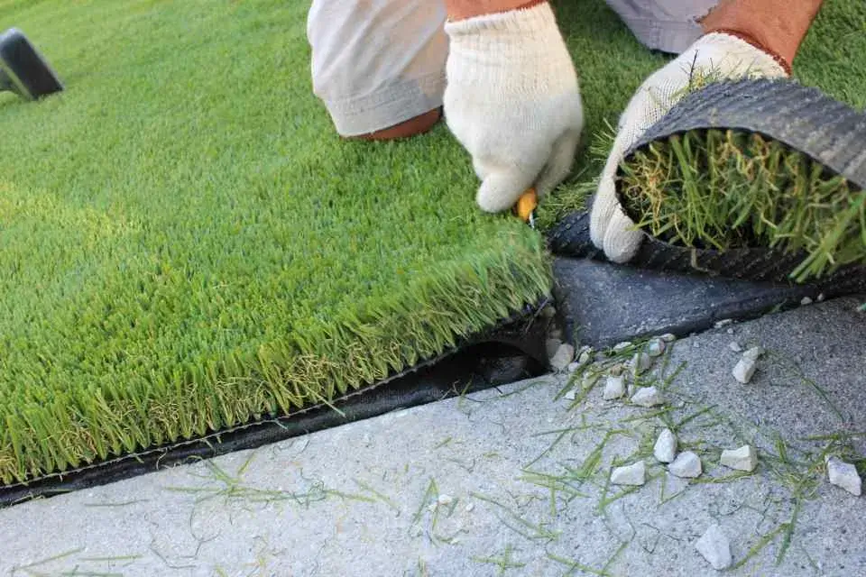 Installer trimming synthetic turf backing with a utility knife over a compacted base